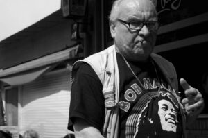 The image features an older man wearing a black shirt with a Bob Marley design on it