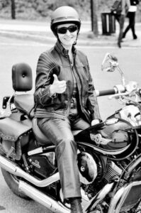 The image features a woman sitting on a motorcycle, giving a thumbs-up sign