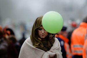 This image shows a person wrapped in a blanket or shawl, holding a green balloon