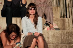 Main Subject: A woman sitting on steps, wearing sunglasses and a denim shirt